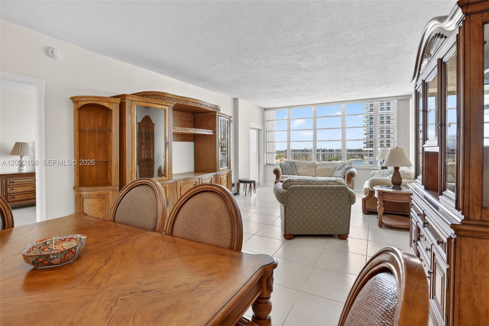 A dining area and living room with tile floors, wooden furniture, and large windows — 1817 S Ocean Dr # 19, Hallandale Beach FL 33009, HALLANDALE BEACH, FL