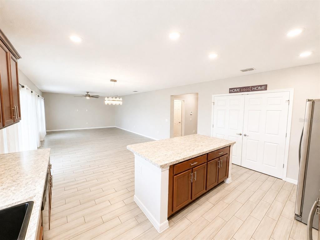 A kitchen with a center island, wood cabinets, and light flooring opens to a living area — 352 BLUE LAKE CIRCLE, KISSIMMEE, FL