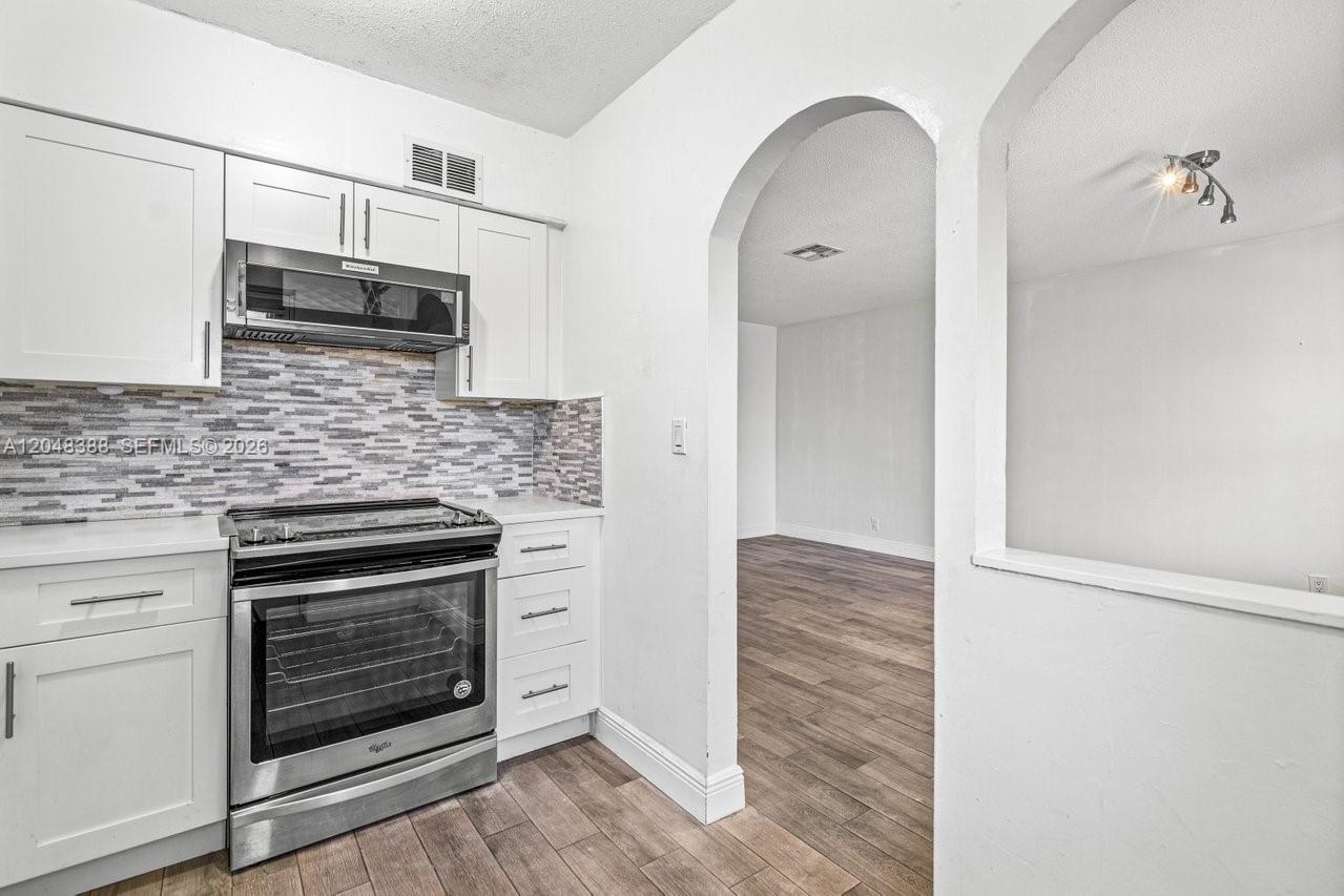 A white kitchen features stainless steel appliances, a tiled backsplash, and an arched doorway — 260 NW 19th St # 26, Boca Raton FL 33432, BOCA RATON, FL