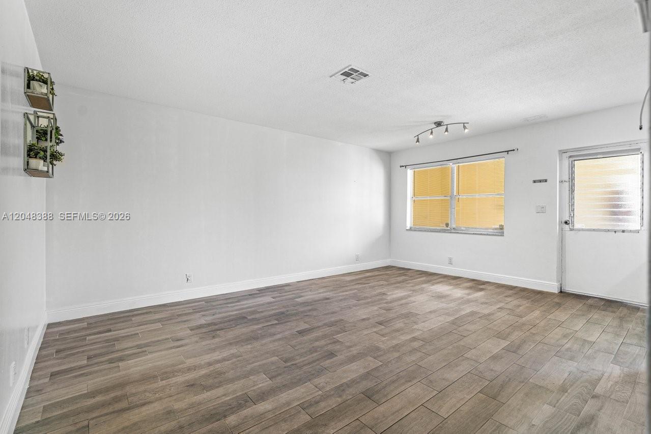 An empty room features wood-look tile flooring, white walls, a window, and a door — 260 NW 19th St # 26, Boca Raton FL 33432, BOCA RATON, FL
