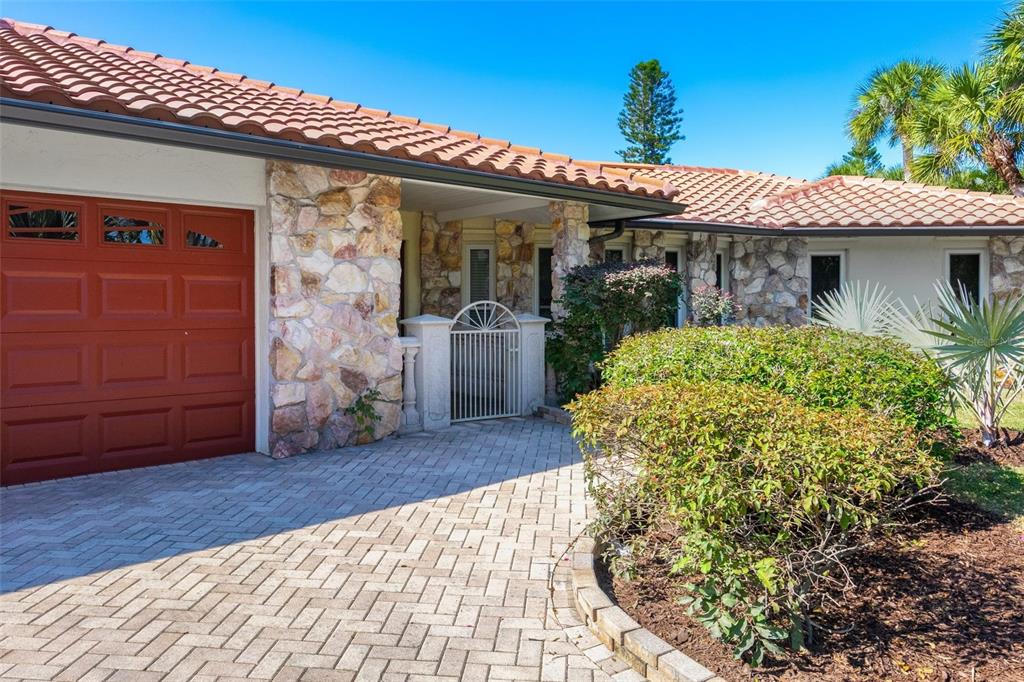 A house exterior features a red garage door, stone facade, and a paved driveway — 5456 AZURE WAY, SARASOTA, FL