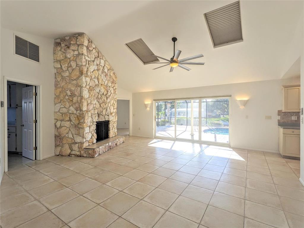 A living room with a stone fireplace, tile flooring, vaulted ceilings, and sliding glass doors — 5456 AZURE WAY, SARASOTA, FL