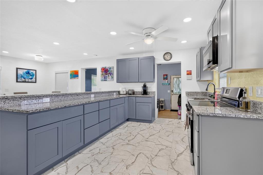A kitchen features blue cabinets, granite countertops, stainless steel appliances, and light-colored marble-look tile flooring — 22018 CATHERINE AVENUE, PORT CHARLOTTE, FL