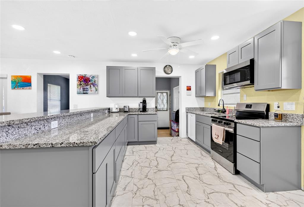 A kitchen features gray cabinets, granite countertops, stainless steel appliances, and white marble-look tile flooring — 22018 CATHERINE AVENUE, PORT CHARLOTTE, FL