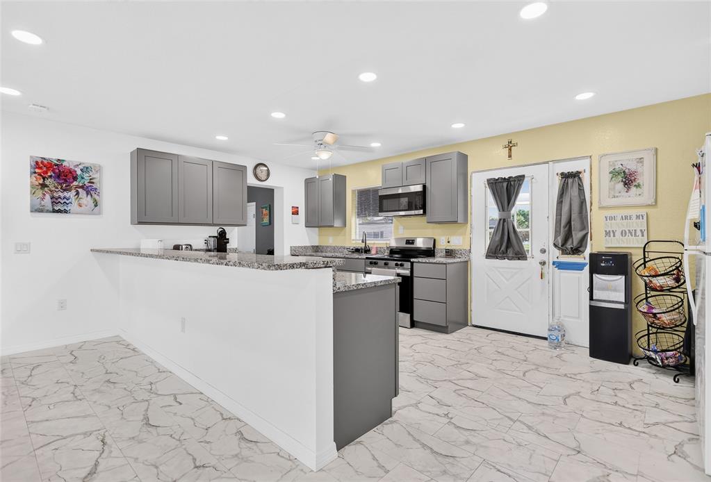 A kitchen features gray cabinets, granite countertops, stainless steel appliances, and white marble-look tile flooring — 22018 CATHERINE AVENUE, PORT CHARLOTTE, FL