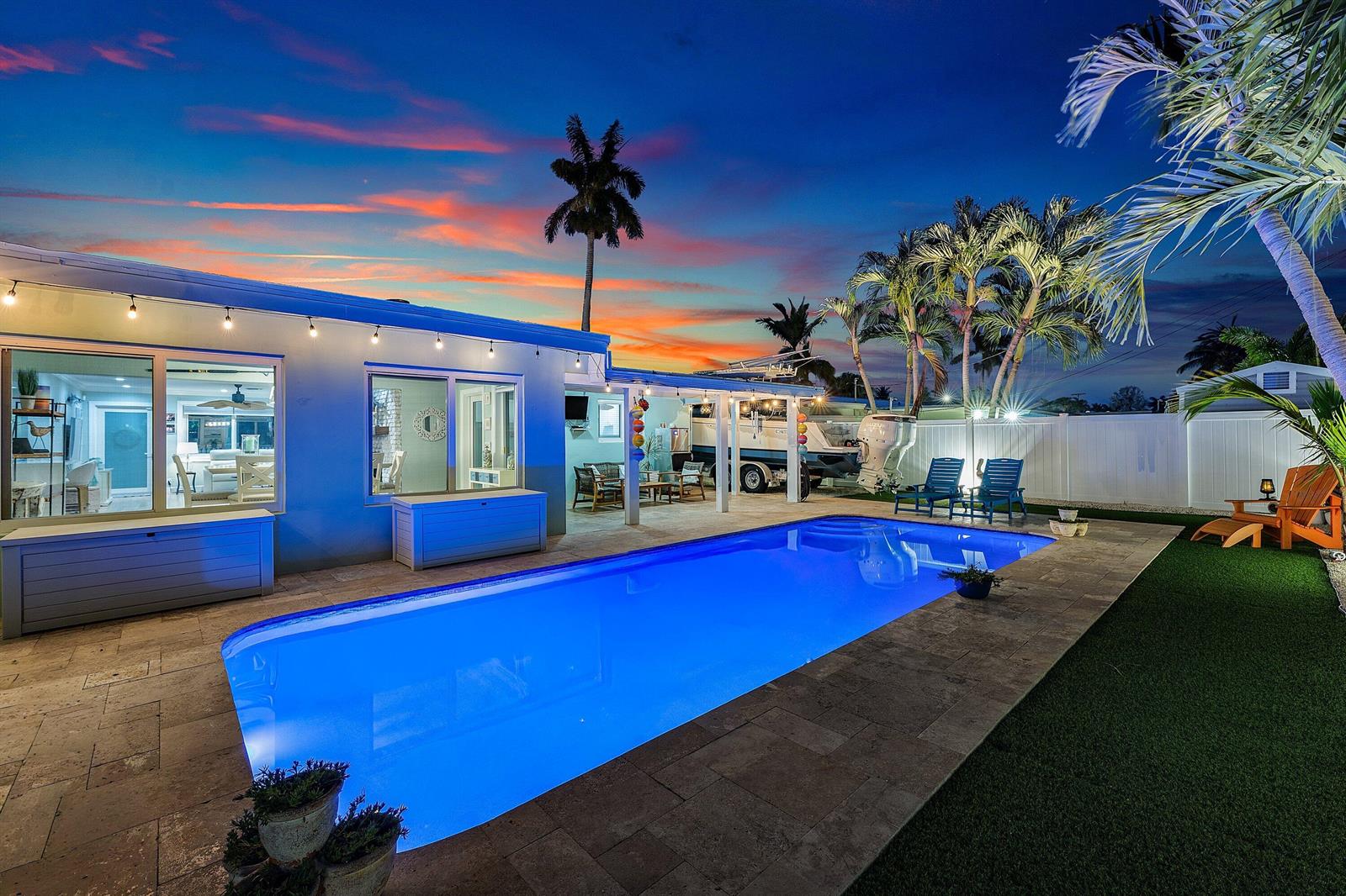 A backyard features a rectangular swimming pool, a covered patio, and palm trees at sunset — 904 SE 15th Court, Deerfield Beach FL 33441, DEERFIELD BEACH, FL