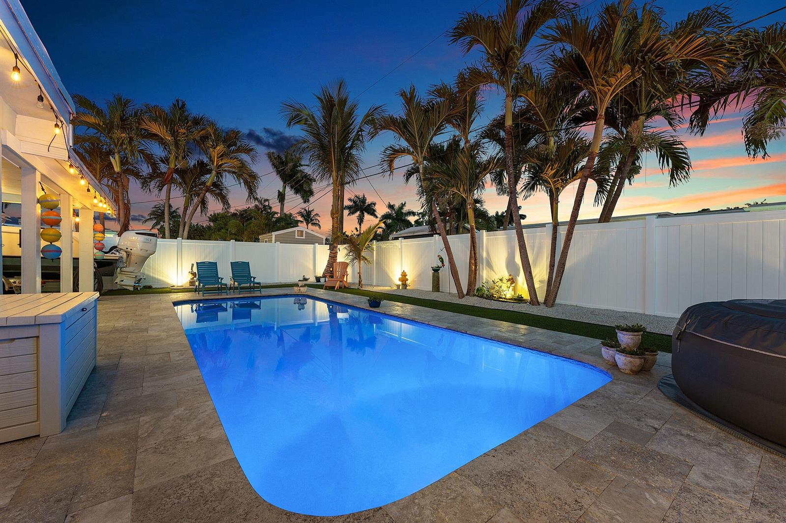 A backyard swimming pool with stone decking, palm trees, and a white privacy fence at dusk — 904 SE 15th Court, Deerfield Beach FL 33441, DEERFIELD BEACH, FL