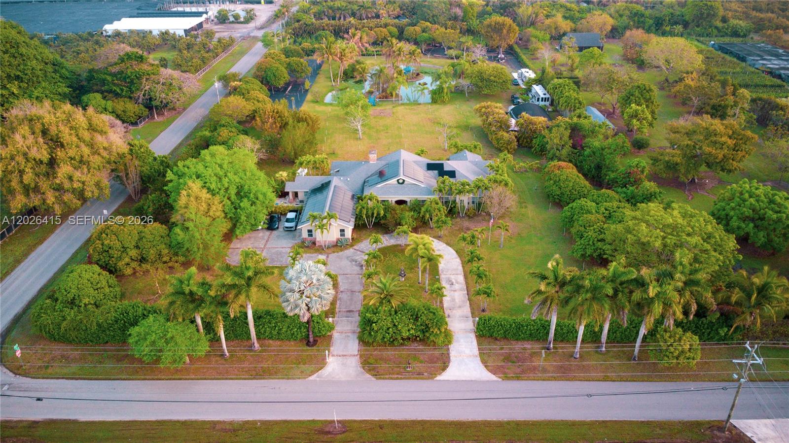 An aerial view shows a house with a circular driveway, palm trees, and a pond — 20175 SW 256th St, Homestead FL 33031, HOMESTEAD, FL