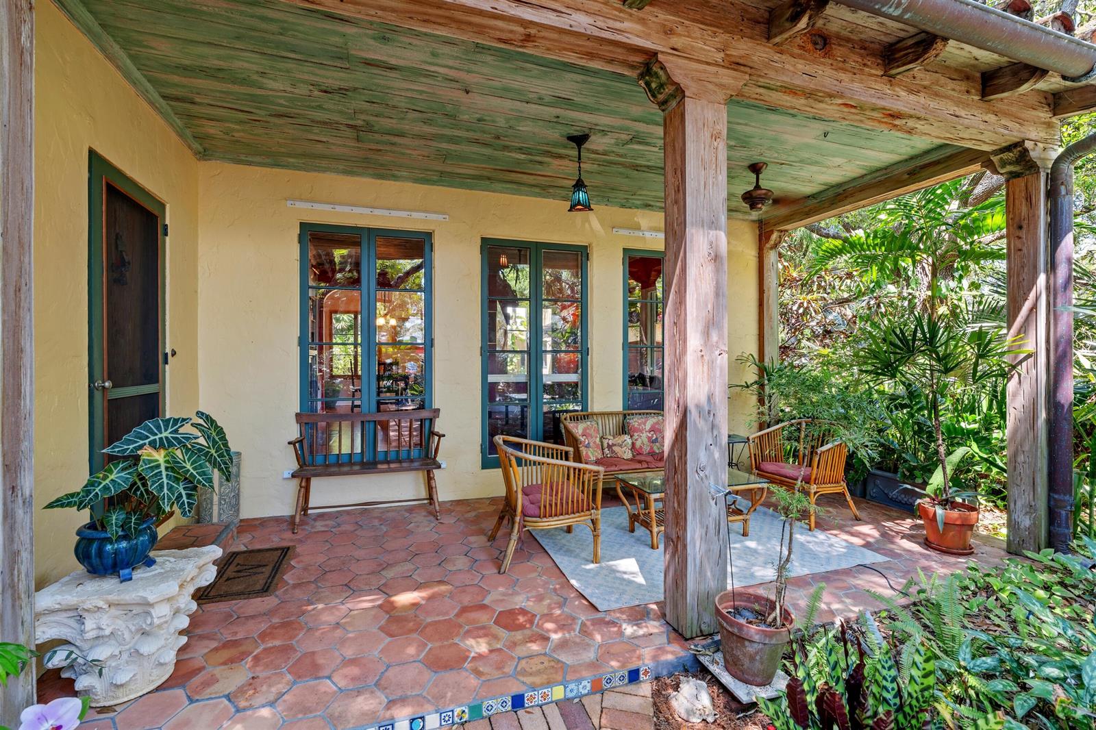 A covered patio features terracotta tile flooring, wooden support beams, and outdoor wicker furniture — 825 Alamanda Street, Boca Raton FL 33486, BOCA RATON, FL