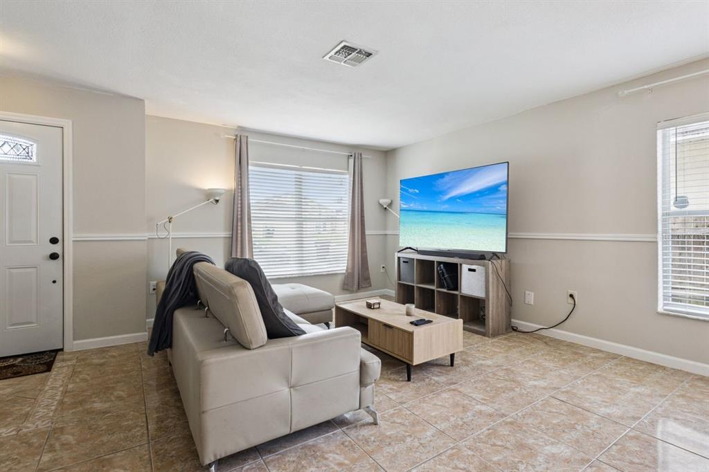 A living room features light tile flooring, a beige sofa, and a television on a stand — 3125 HOLLAND DRIVE, ORLANDO, FL
