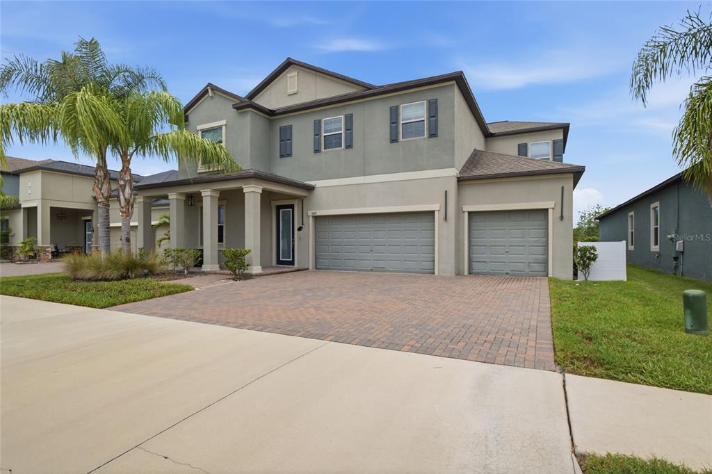 A two-story suburban house with a paver driveway, three-car garage, and a covered front porch — 11419 SUNBURST MARBLE ROAD, RIVERVIEW, FL