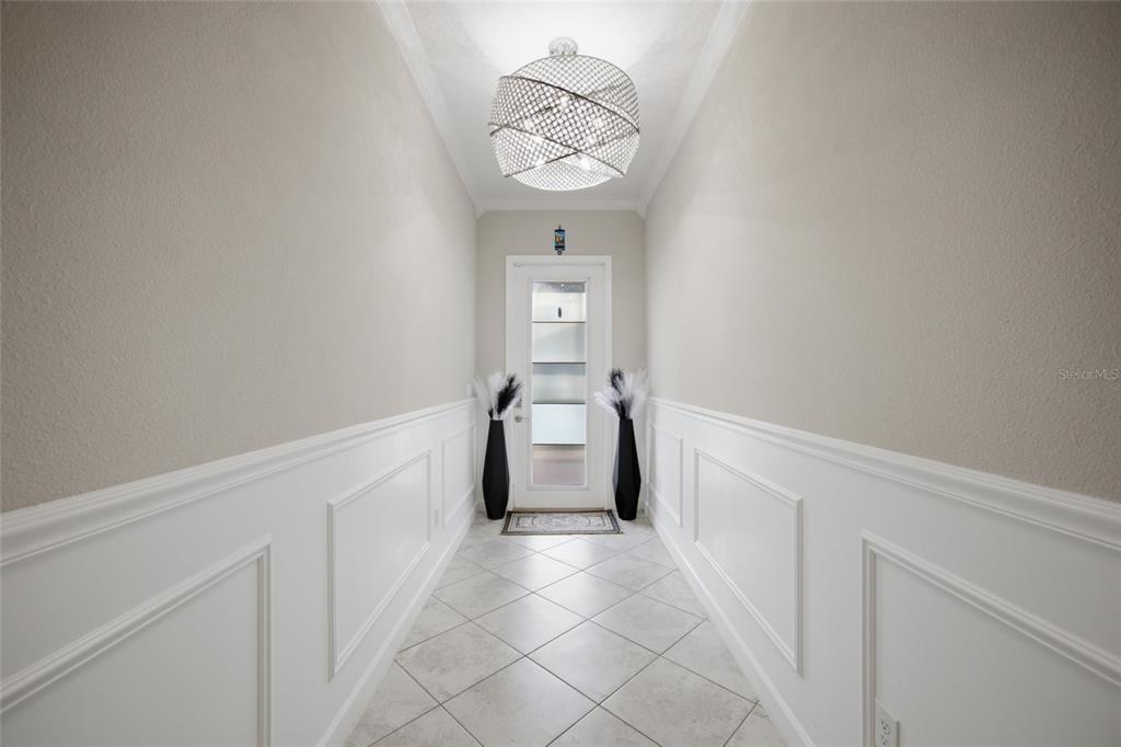A hallway features white wainscoting, tiled floors, a modern chandelier, and a glass-paneled front door — 11419 SUNBURST MARBLE ROAD, RIVERVIEW, FL
