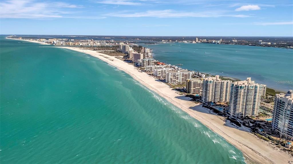 An aerial view shows a sandy beach lined with high-rise condominiums along the coastline — 1400 GULF BOULEVARD UNIT 101, CLEARWATER BEACH, FL