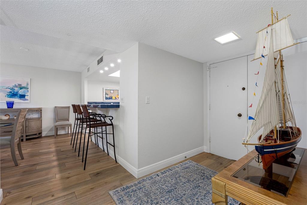 A room with wood-look flooring, a breakfast bar with stools, and a large model ship — 1400 GULF BOULEVARD UNIT 101, CLEARWATER BEACH, FL