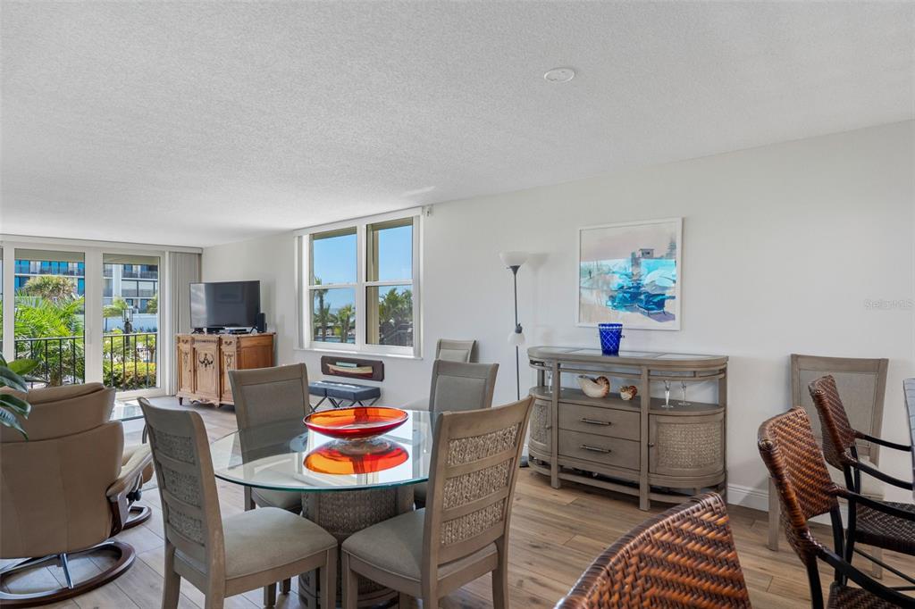 A dining area with a glass table, wicker chairs, and a wooden sideboard near a balcony — 1400 GULF BOULEVARD UNIT 101, CLEARWATER BEACH, FL