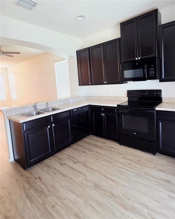 A kitchen features dark wood cabinets, black appliances, and light-colored countertops over wood-look flooring — 8821 WALNUT GABLE COURT, RIVERVIEW, FL