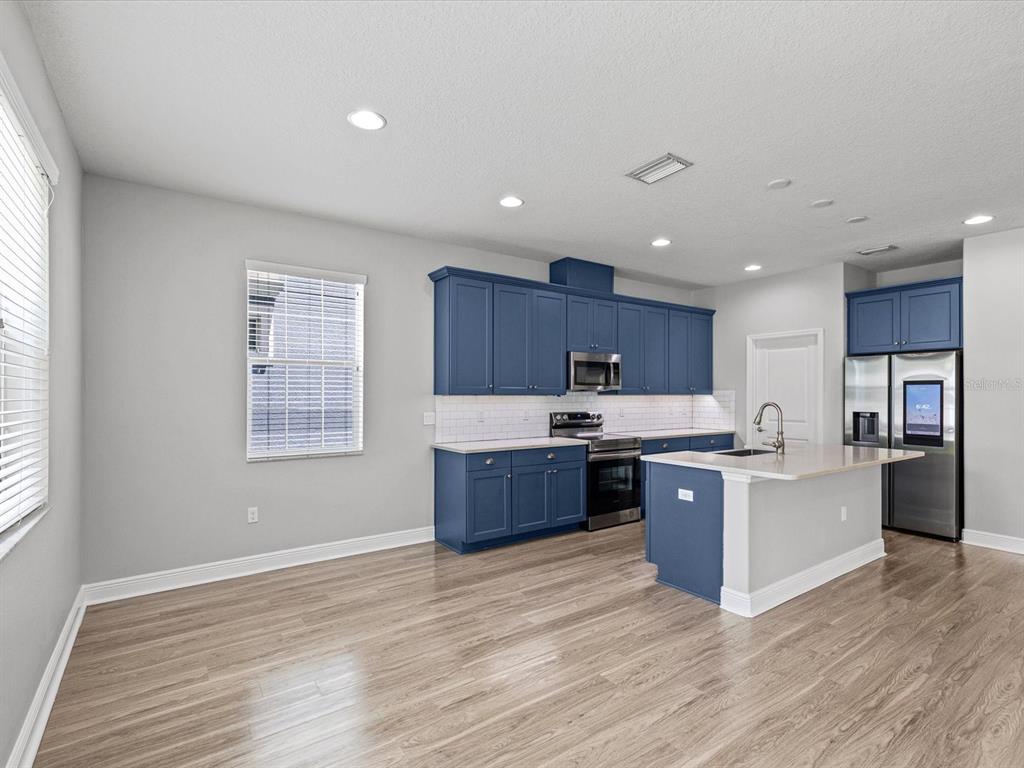 A kitchen features blue cabinets, stainless steel appliances, a center island, and light wood flooring — 7105 PARK TREE DRIVE, TAMPA, FL