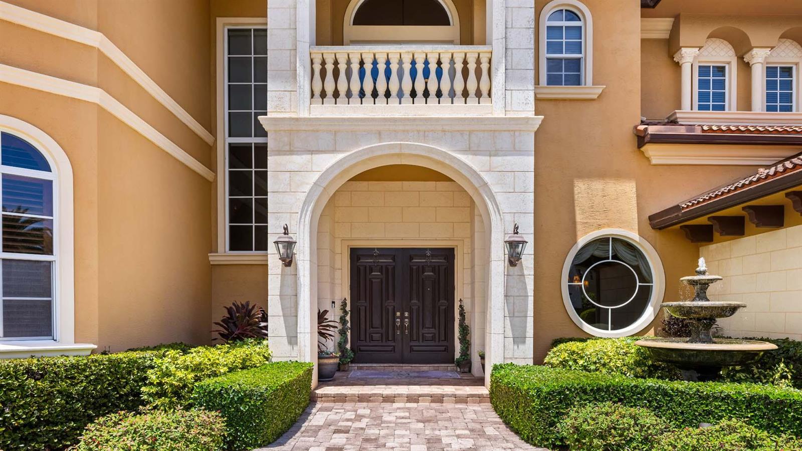 A stone-arched entryway with double doors, a balcony, and a tiered fountain in the foreground — 929 Banyan Drive, Delray Beach FL 33483, DELRAY BEACH, FL
