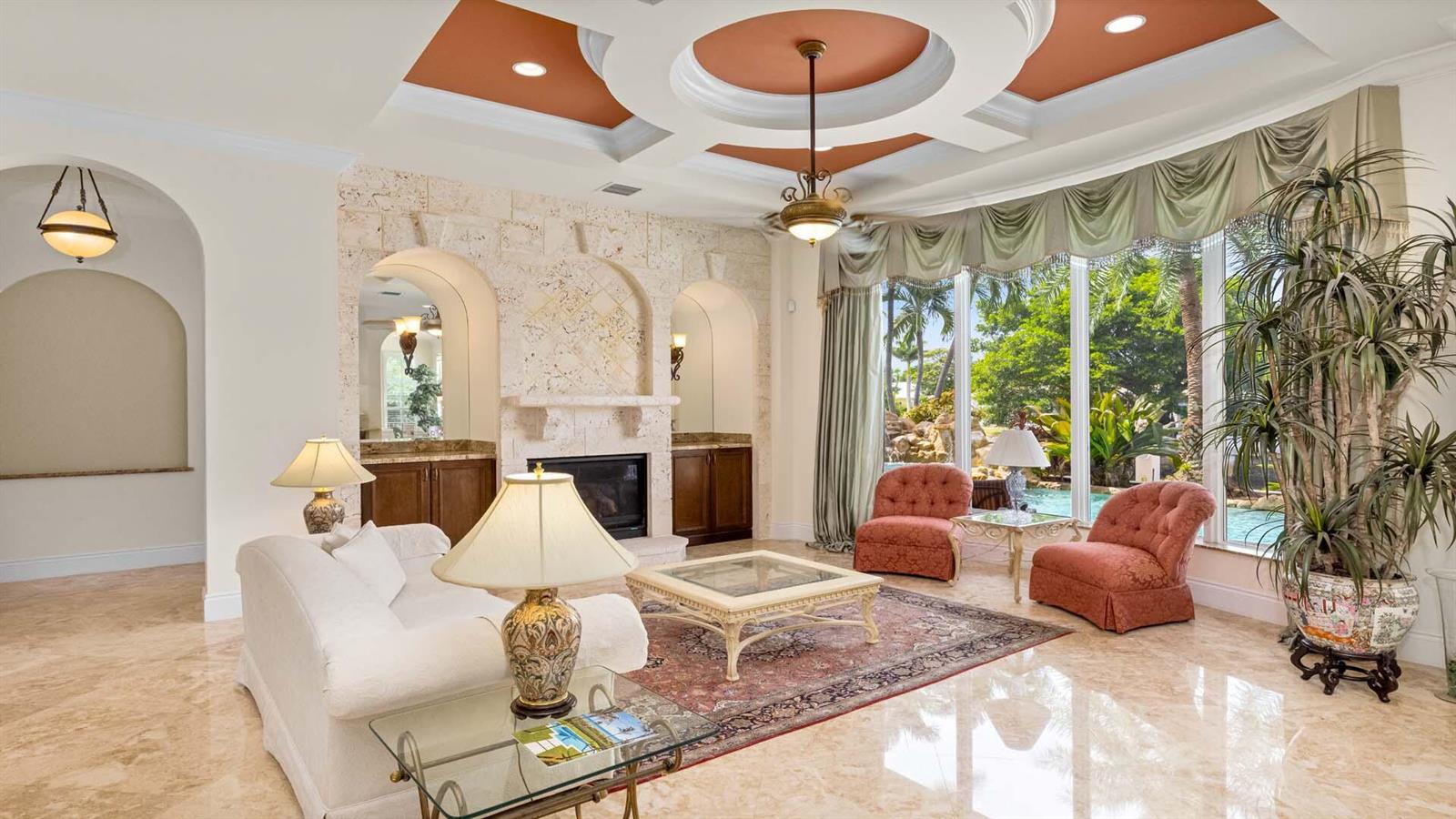 A living room features a stone fireplace, coffered ceiling, tile floors, and large windows — 929 Banyan Drive, Delray Beach FL 33483, DELRAY BEACH, FL