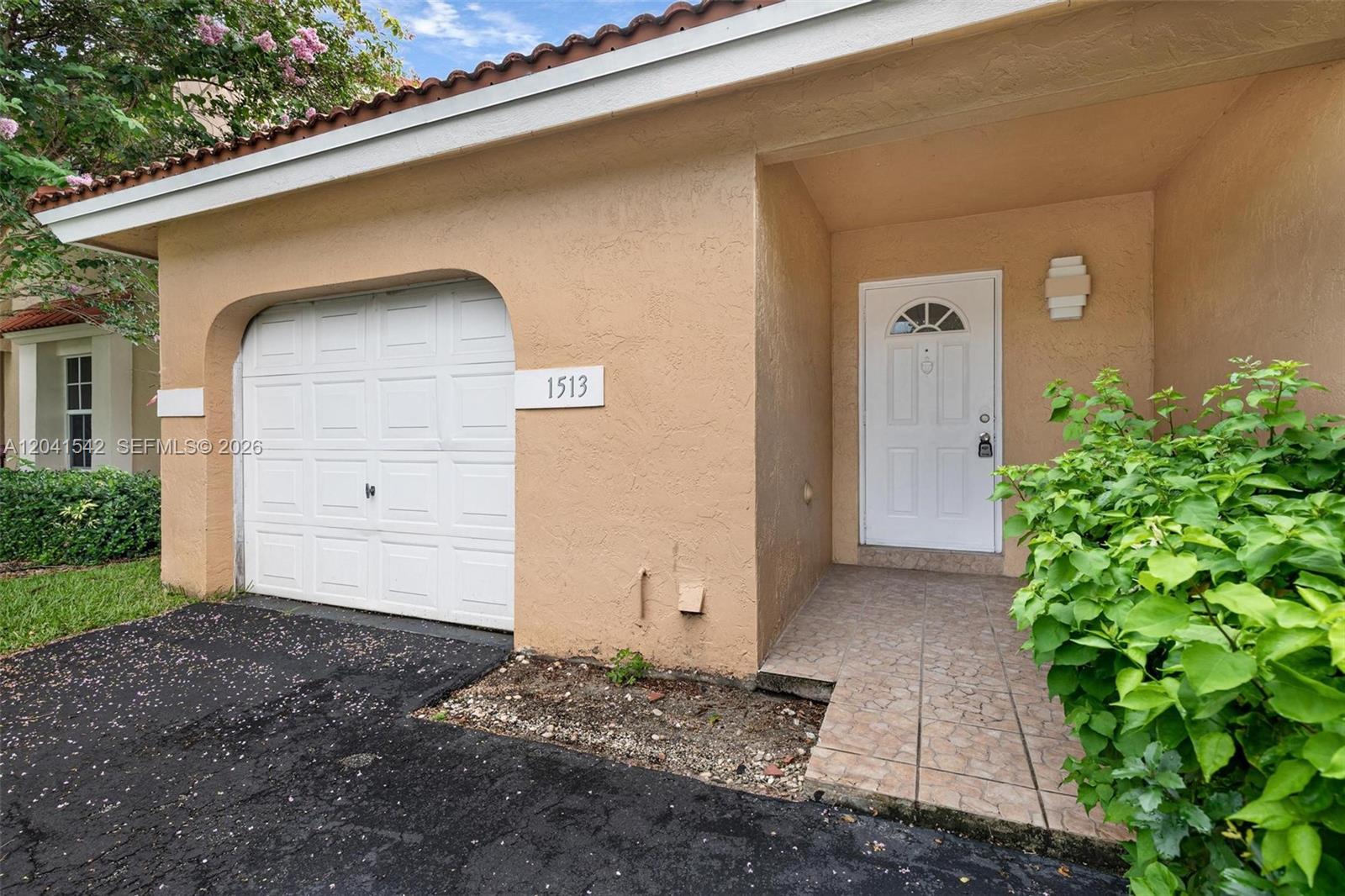 The exterior view shows a beige stucco home with a white garage door and entryway — 1513 Garden Rd, Weston FL 33326, WESTON, FL