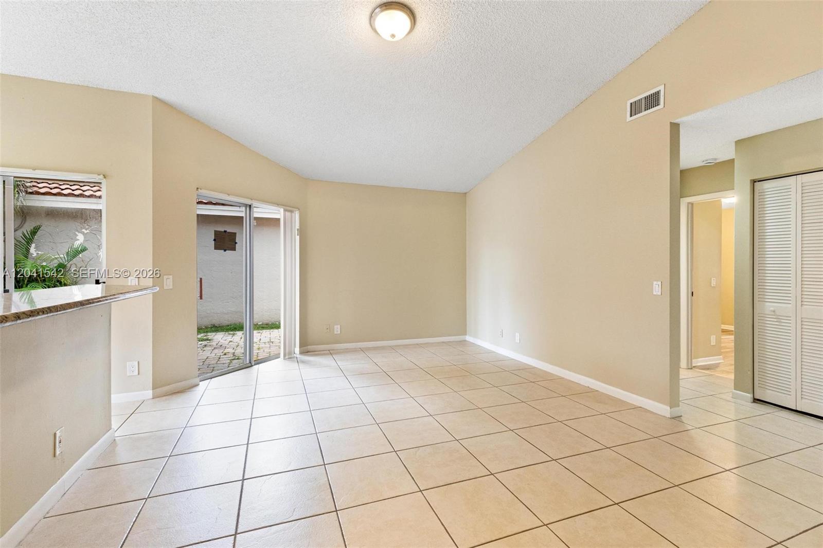 An empty room features beige walls, light-colored tile flooring, a vaulted ceiling, and sliding glass doors — 1513 Garden Rd, Weston FL 33326, WESTON, FL