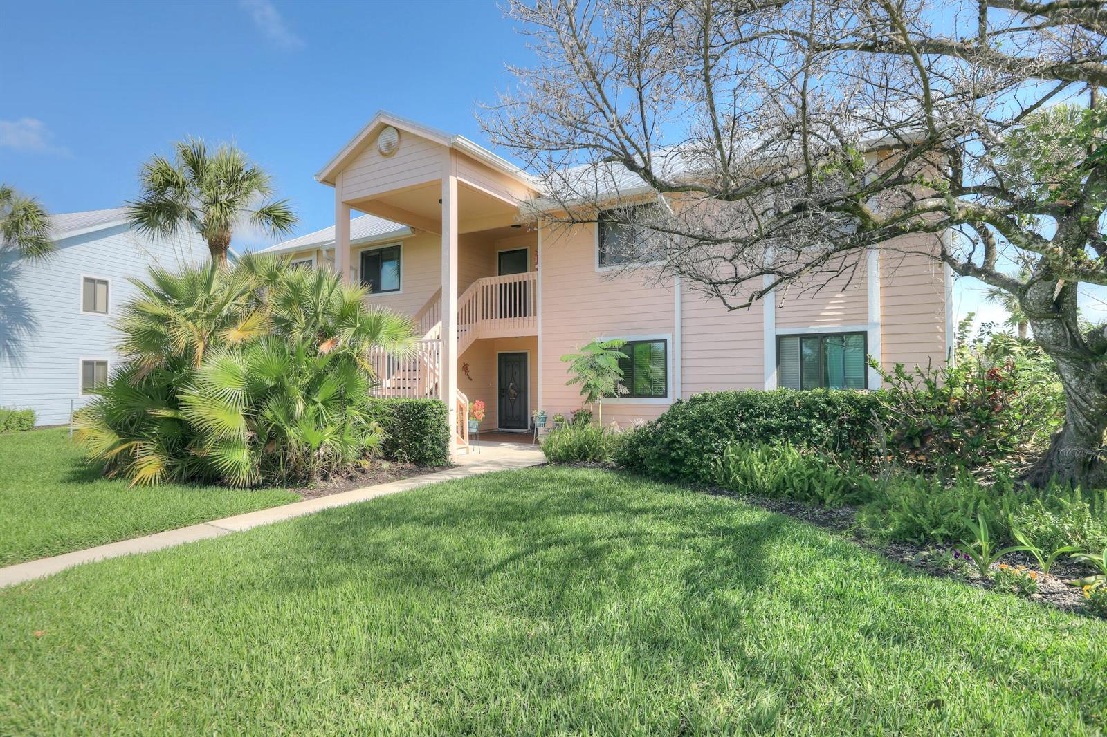 A two-story peach-colored house with a covered entryway and stairs surrounded by landscaped greenery — 5720 Pelican Pointe Drive # 3, Sebastian FL 32958, SEBASTIAN, FL