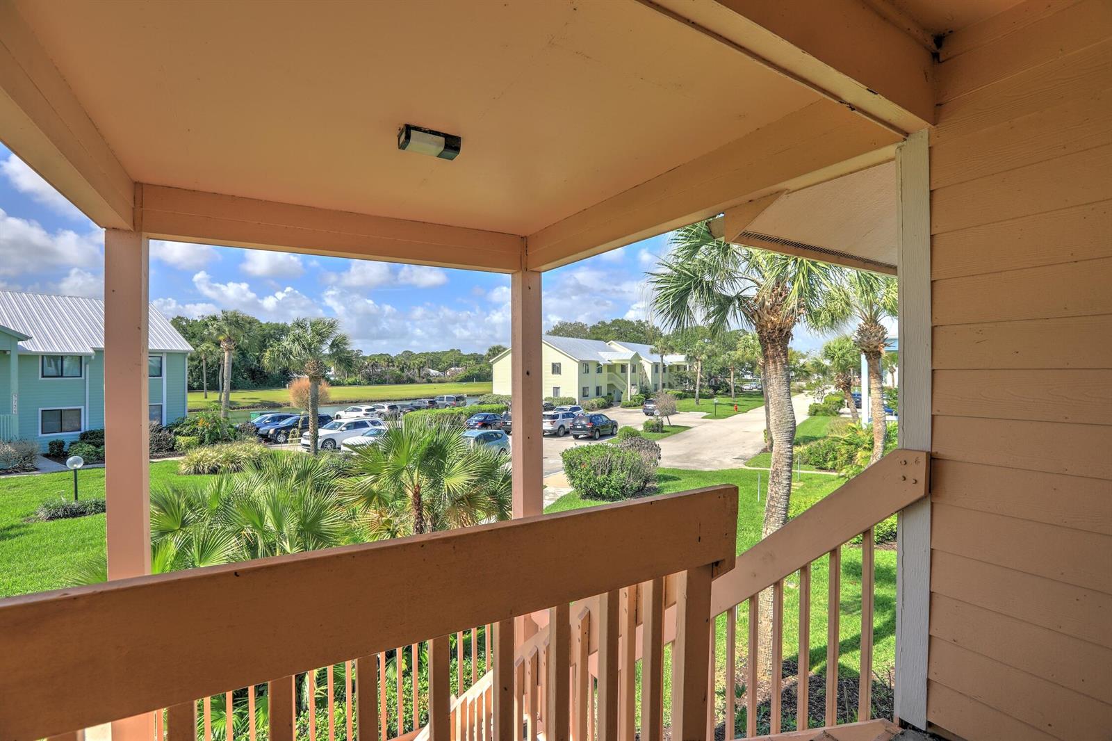 A view from a wooden balcony overlooking a parking lot, palm trees, and apartment buildings — 5720 Pelican Pointe Drive # 3, Sebastian FL 32958, SEBASTIAN, FL