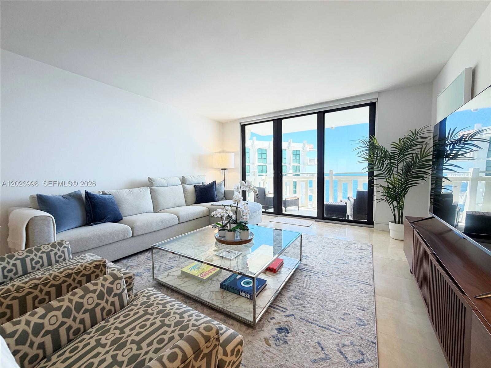 A living room features a light-colored sectional sofa, a glass coffee table, and balcony views — 1111 Crandon Blvd # B1105, Key Biscayne FL 33149, KEY BISCAYNE, FL