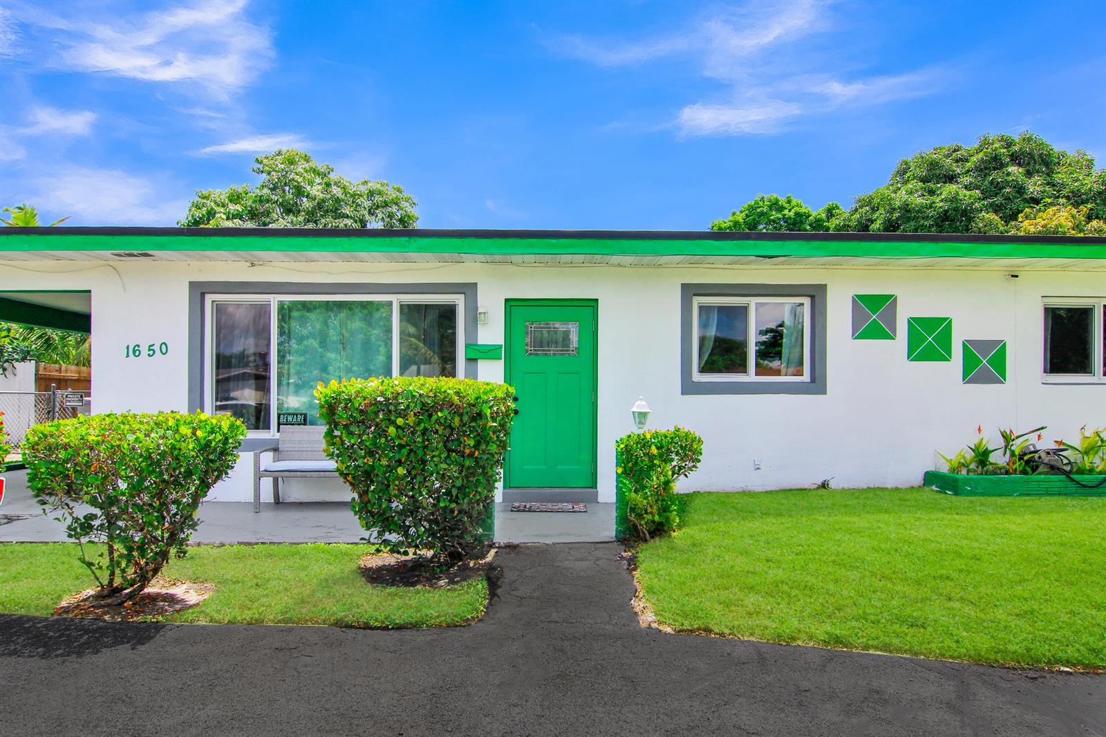 A white house exterior features a green-painted carport, a gray front door, and a small lawn — 1650 NW 1st Way, Pompano Beach FL 33060, POMPANO BEACH, FL