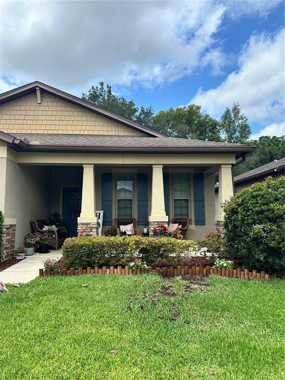 A single-story house features a covered front porch with columns, wicker furniture, and landscaping — 15541 STONE HOUSE DRIVE, BROOKSVILLE, FL