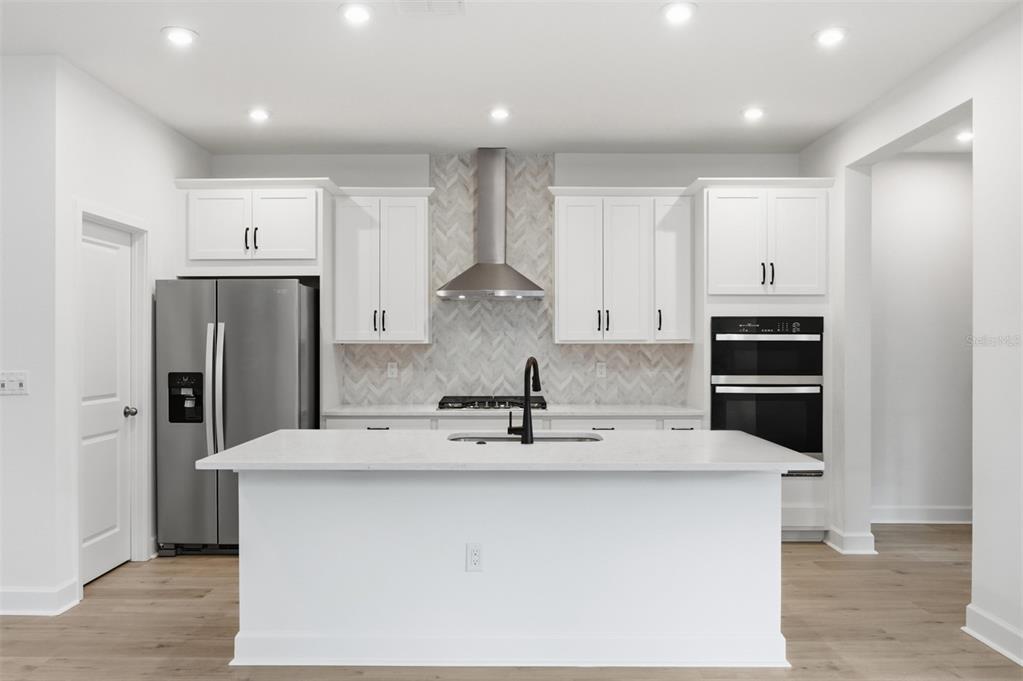 A modern kitchen features white cabinetry, a central island, stainless steel appliances, and herringbone backsplash — 1943 SEAWALL WAY, CELEBRATION, FL