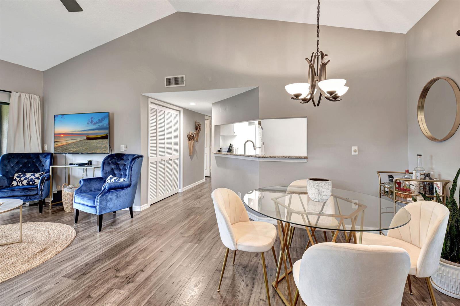 A living and dining area with gray walls, wood-look flooring, blue chairs, and glass table — 22 Via De Casas Sur # 101, Boynton Beach FL 33426, BOYNTON BEACH, FL