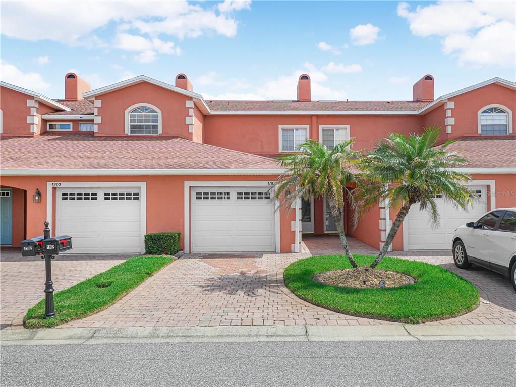 A row of attached townhomes with terracotta-colored stucco, white garage doors, and paver driveways — 1102 ASHTON PALMS DRIVE, LAKE WALES, FL