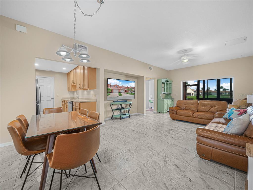 An open-concept living and dining area features tile flooring, leather furniture, and a kitchen nook — 1102 ASHTON PALMS DRIVE, LAKE WALES, FL