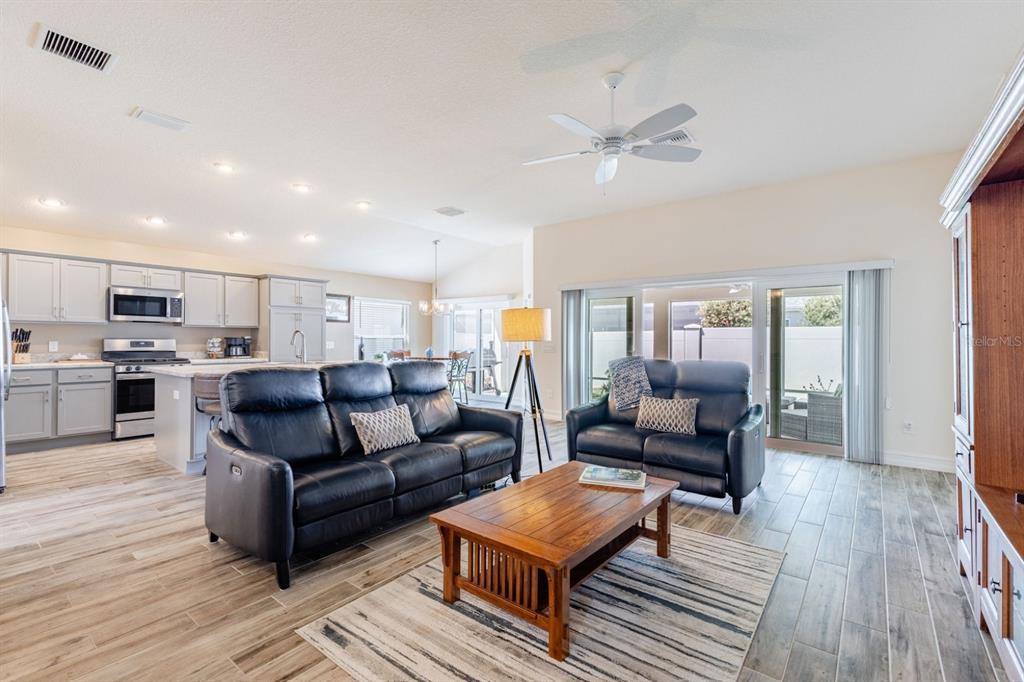 An open-concept living room with gray cabinets, dark leather sofas, and wood-look tile flooring — 580 GOUGH PLACE, THE VILLAGES, FL