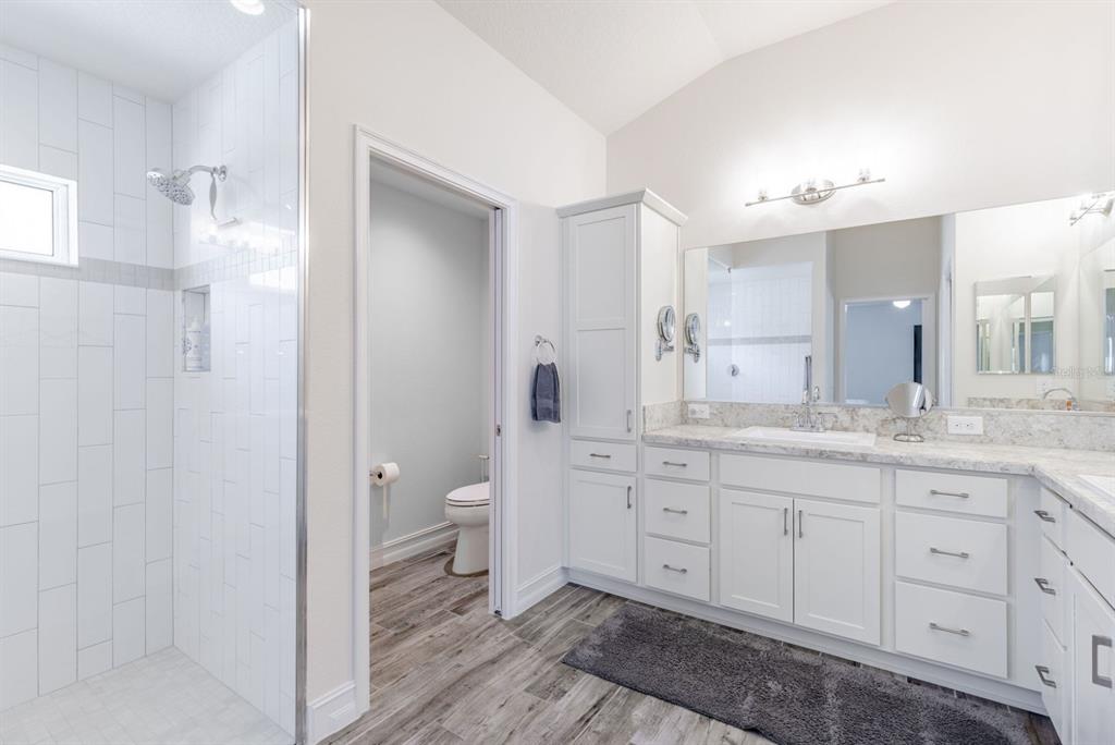 A bathroom features a glass-enclosed shower, white cabinetry, a double vanity, and wood-look flooring — 580 GOUGH PLACE, THE VILLAGES, FL