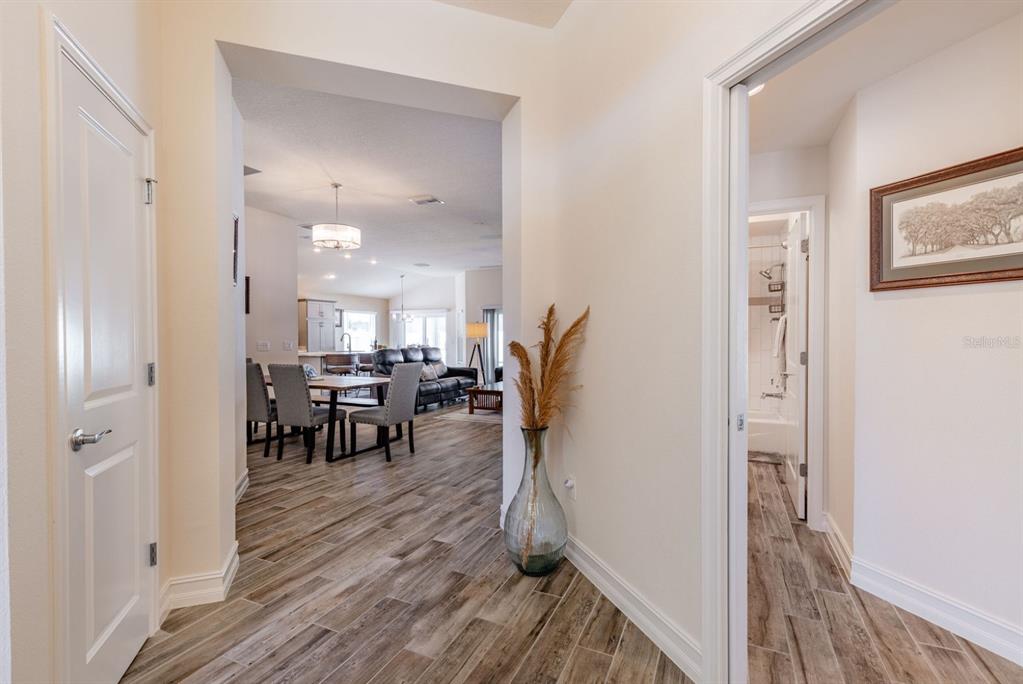 A hallway with wood-look tile flooring leads into an open-concept dining and living area — 580 GOUGH PLACE, THE VILLAGES, FL