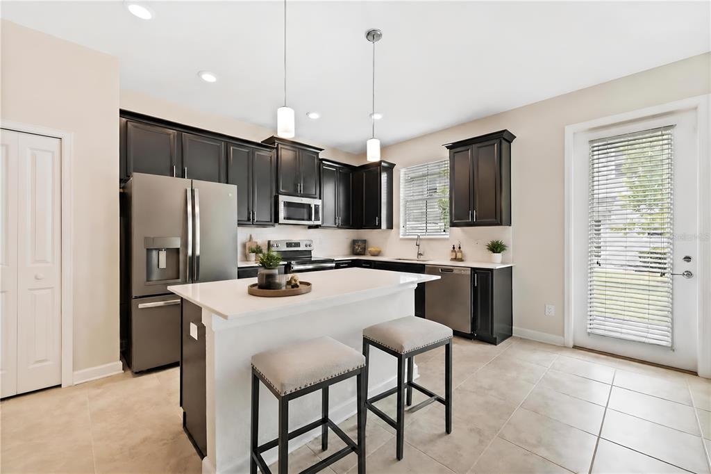 A kitchen features dark cabinets, stainless steel appliances, a white island, and light tile flooring — 2935 THEME STREET, KISSIMMEE, FL