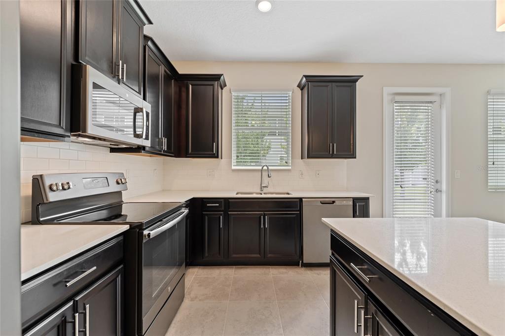 A kitchen features dark wood cabinets, white countertops, stainless steel appliances, and a center island — 2935 THEME STREET, KISSIMMEE, FL