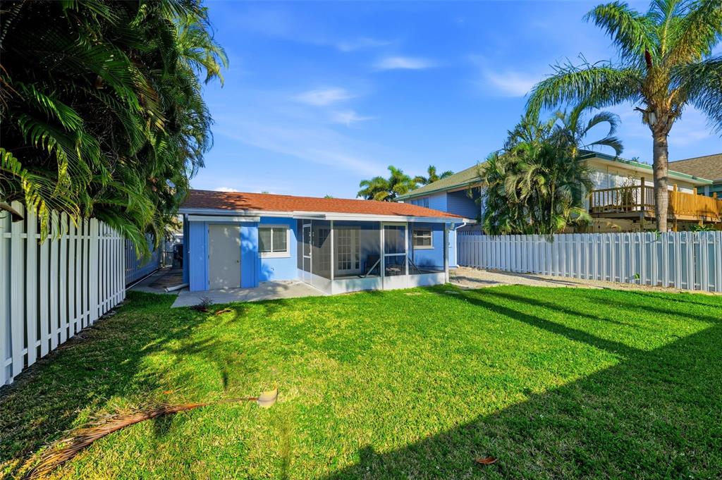 A blue house with a screened-in porch sits in a backyard with a white fence — 17734 1ST STREET E, REDINGTON SHORES, FL
