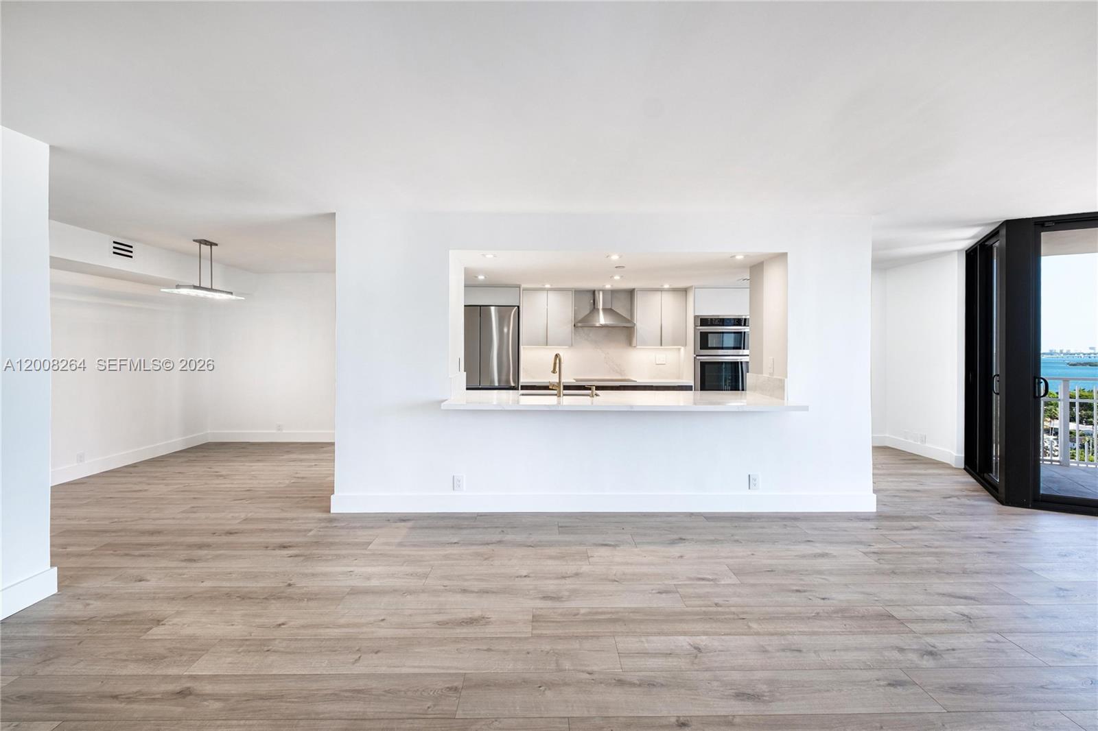 A bright, open-concept living area features light wood flooring and a pass-through kitchen window — 2000 Towerside Ter # 1506, Miami FL 33138, MIAMI, FL