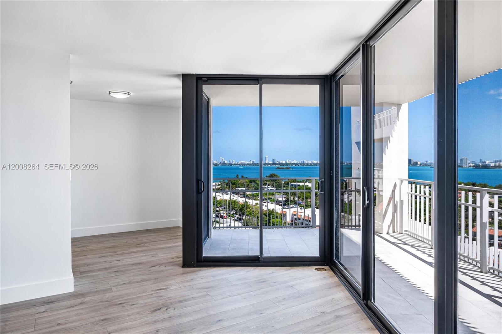 An empty room with light wood-look flooring features floor-to-ceiling glass doors opening to a balcony — 2000 Towerside Ter # 1506, Miami FL 33138, MIAMI, FL
