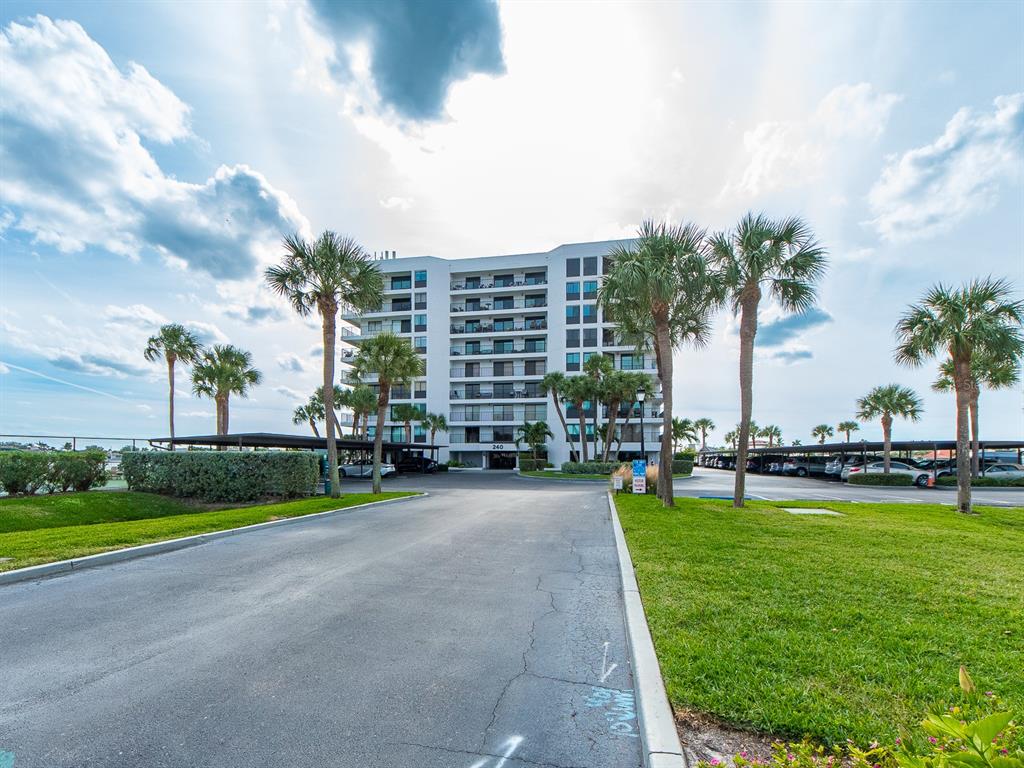A multi-story apartment building stands at the end of a paved driveway with palm trees — 240 SAND KEY ESTATES DRIVE UNIT 216, CLEARWATER BEACH, FL