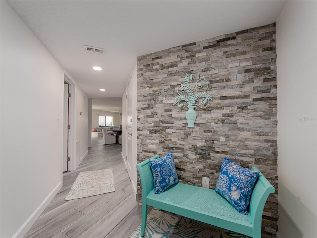A hallway features a stone accent wall, a teal bench, and light wood-look flooring — 240 SAND KEY ESTATES DRIVE UNIT 216, CLEARWATER BEACH, FL