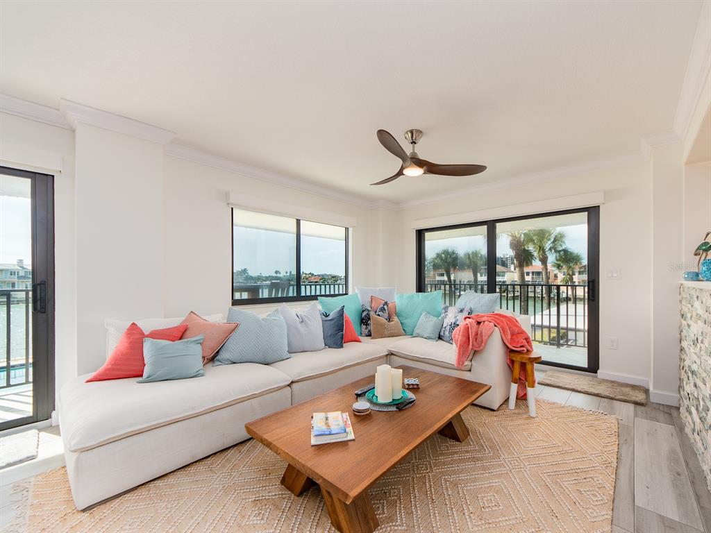A living room features a white sectional sofa, wooden coffee table, and sliding glass doors — 240 SAND KEY ESTATES DRIVE UNIT 216, CLEARWATER BEACH, FL