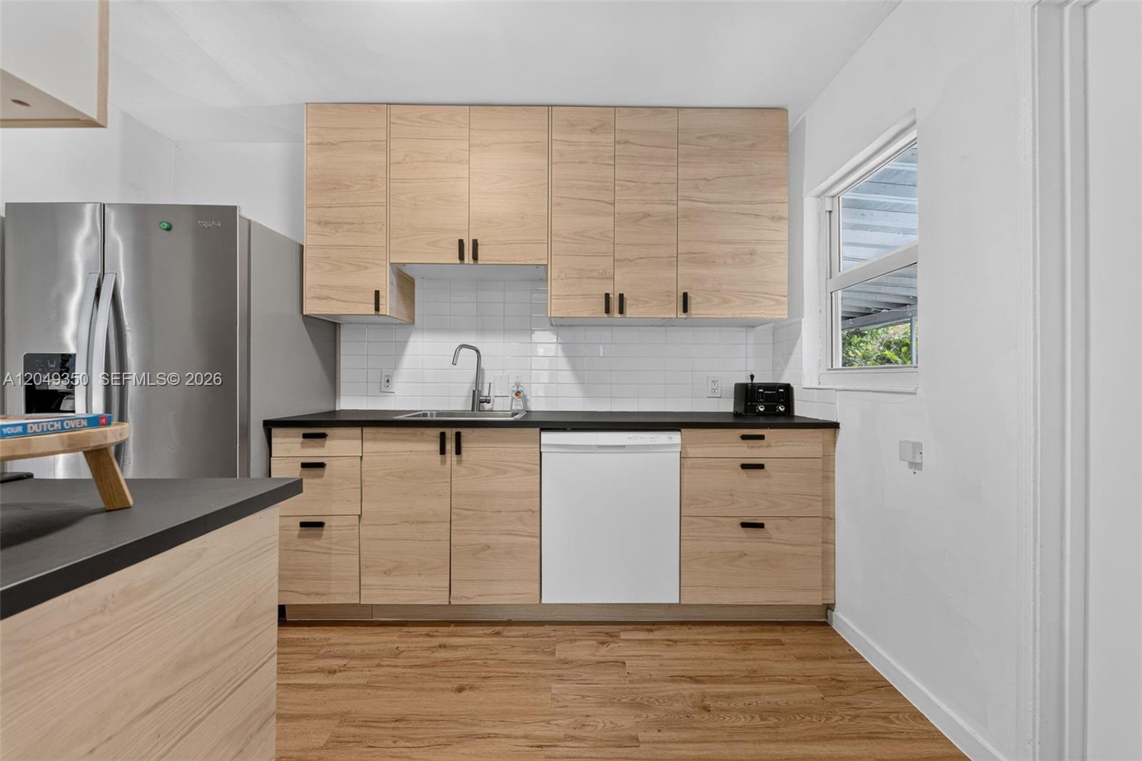 A kitchen features light wood cabinets, black countertops, a white dishwasher, and a subway tile backsplash — 5800 SW 61st St, Miami FL 33143, MIAMI, FL