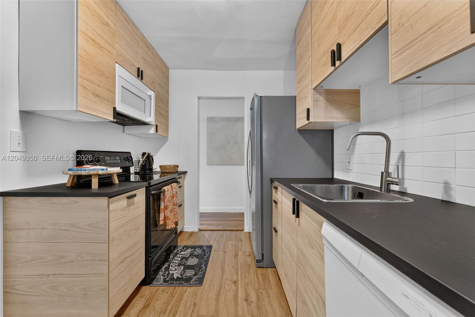 This galley kitchen features light wood cabinets, black countertops, and stainless steel appliances — 5800 SW 61st St, Miami FL 33143, MIAMI, FL