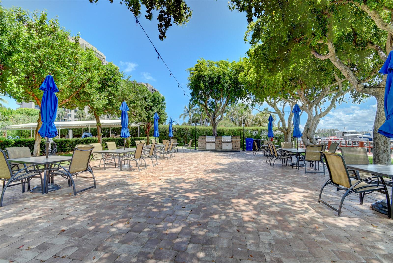 An outdoor patio features dining tables with blue umbrellas, chairs, and built-in stone grills — 2121 N Ocean Boulevard # 1406w, Boca Raton FL 33431, BOCA RATON, FL