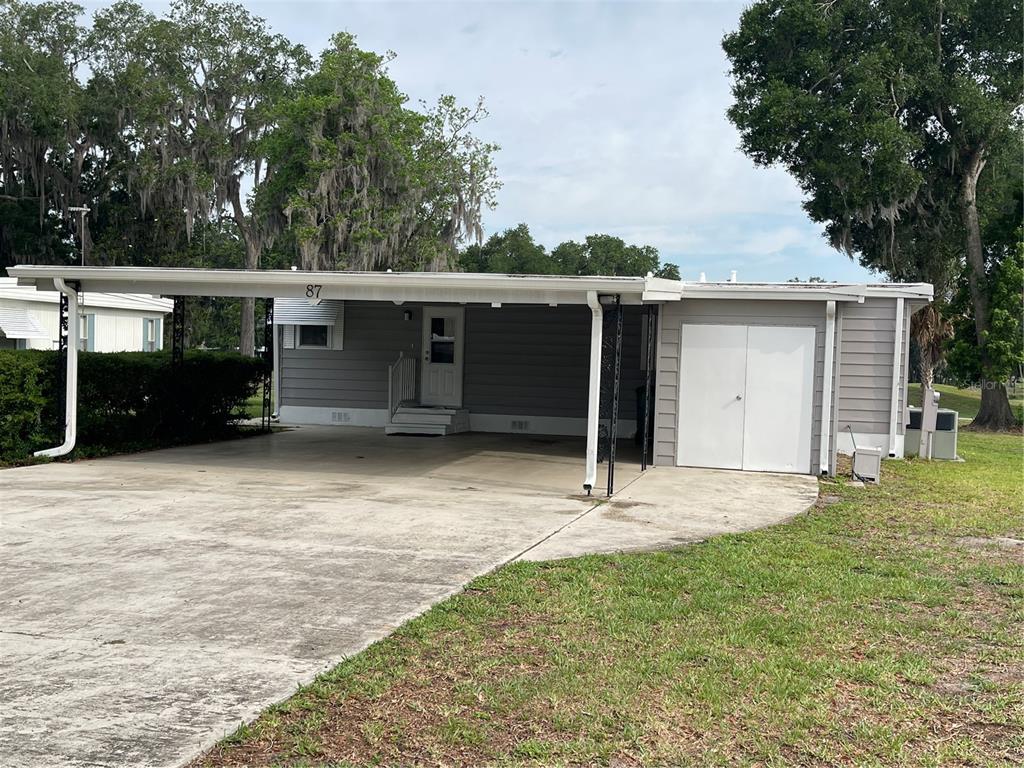 A gray mobile home with a large concrete driveway, a carport, and an attached storage shed — 87 N BOBWHITE ROAD, WILDWOOD, FL
