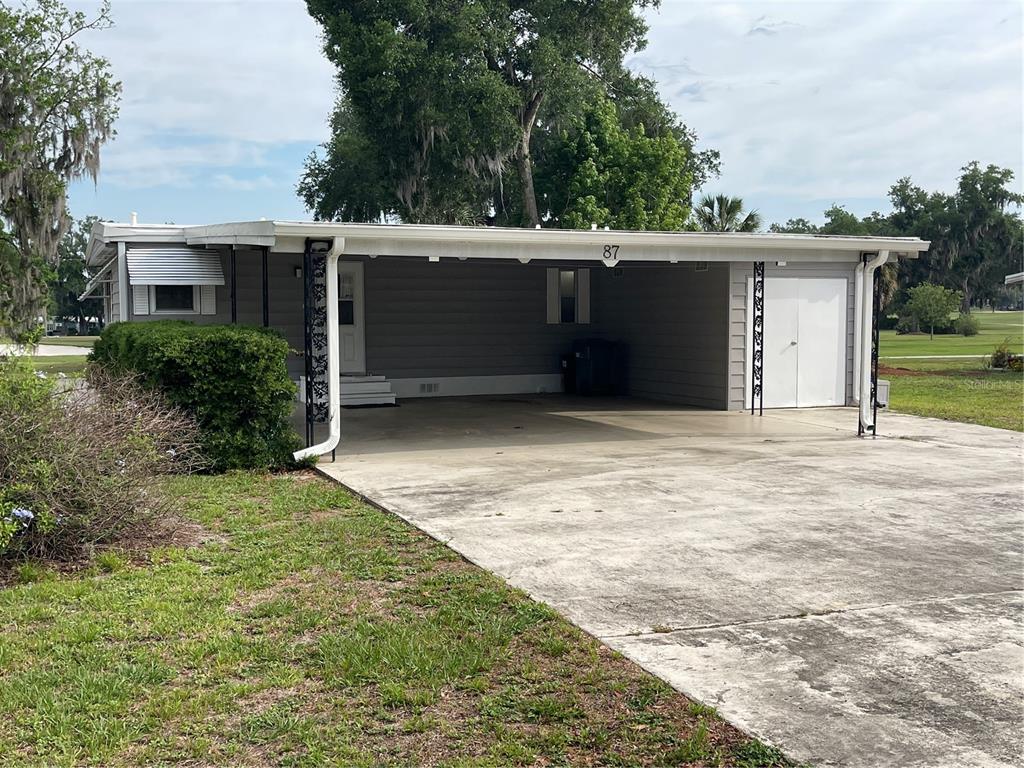 A single-story house with a gray exterior, a large carport, and a concrete driveway — 87 N BOBWHITE ROAD, WILDWOOD, FL